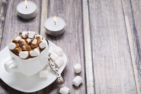 棉花糖在白色杯和两个木制的桌子上的蜡烛热巧克力