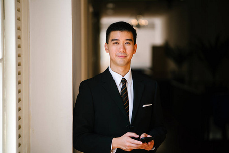 年轻英俊的中国亚裔男子在西装与他的智能手机的肖像照片