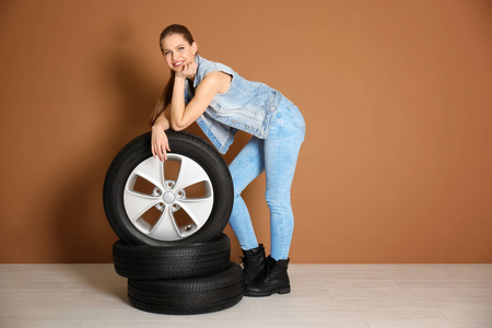 在彩色墙壁背景的汽车轮胎诱人的装备的年轻妇女