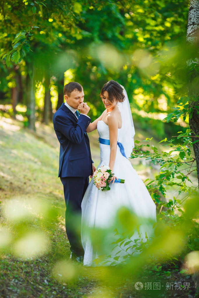 穿西装的新郎在阳光明媚的森林亲吻新娘的手