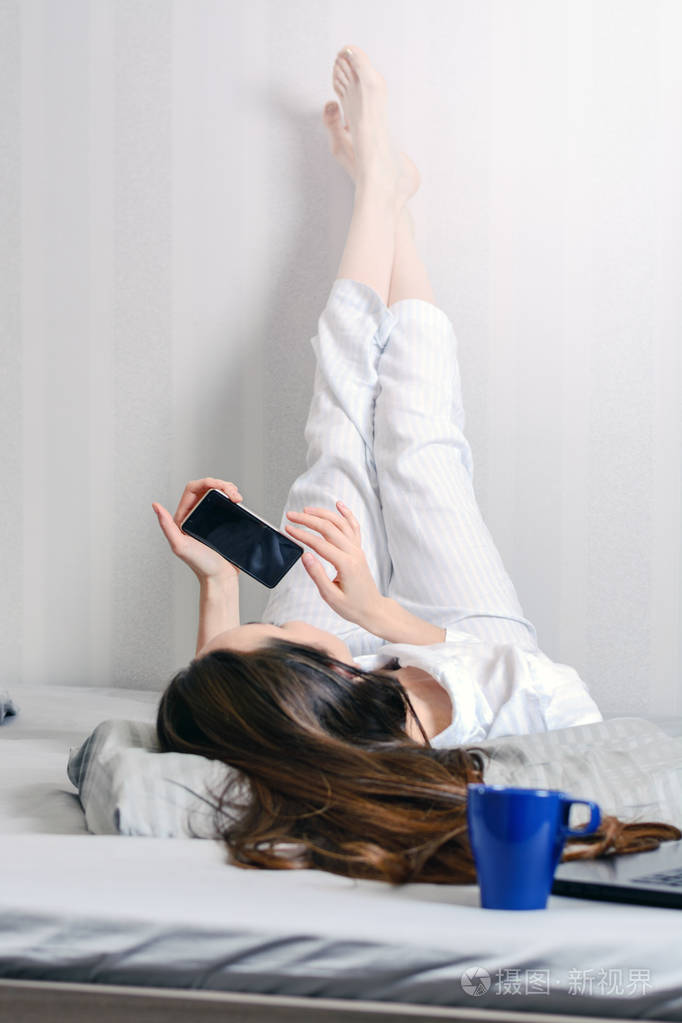 穿着睡衣的年轻女子躺在床上, 脚在墙上.