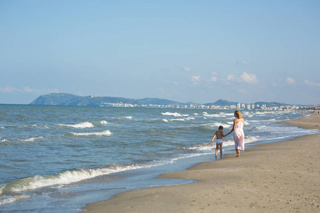 快乐美丽的年轻妈妈和孩子沿着海边走很远