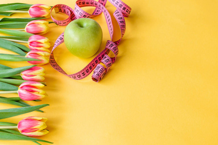 郁金香, 绿色苹果和磁带措施在黄色背景。春季排毒减肥和身体提神的概念