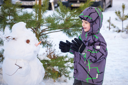 搞笑小小孩男孩做雪人和吃胡萝卜，玩玩雪，在户外对寒冷的一天。积极的休闲儿童冬季