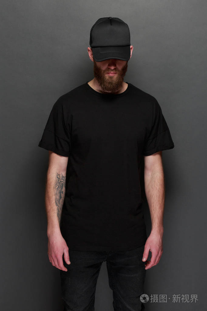 时髦英俊的男性模特与胡子穿着黑色空白 t恤和黑色棒球帽与空间为您的
