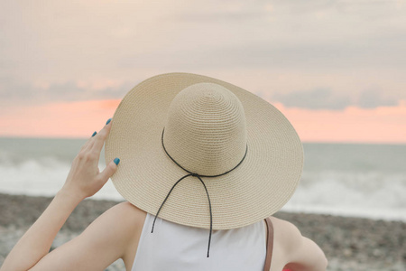 戴着帽子的女孩坐在海边。后退视图。特写