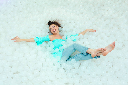 快乐的美丽的女人奠定周围的白色塑料球在干燥池为成人