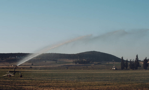 喷水灭火装置在现场以蓝天为背景。灌溉系统在绿色领域的作用。农业和技术概念