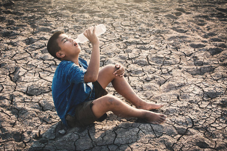 哀伤的男孩饮用水在裂缝地面, 概念干旱和缺水危机照片