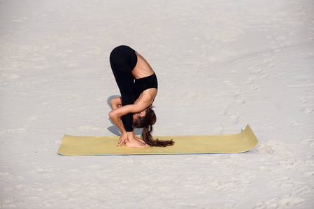 健身女孩在海滩上伸展运动。女运动员在瑜伽垫上做热身运动。运动瑜伽与健康生活方式概念