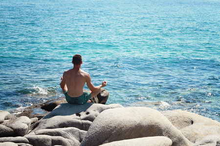 坐在岩石上做瑜伽的人坐在海边冥想
