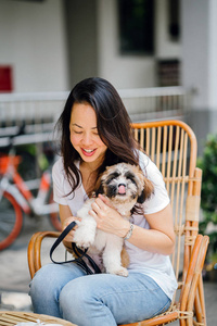 年轻的泛亚洲妇女享受她的周末与她的宠物石 tzuh 狗。她坐在阳光下的藤椅上, 和她的狗一起在咖啡馆里。