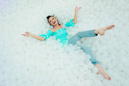 快乐的美丽的女人奠定周围的白色塑料球在干燥池为成人