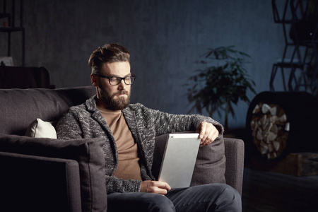 有吸引力优雅经典帅哥穿着时髦灰色和眼镜，留着胡子，坐在笔记本电脑时尚深色内饰豪华家具