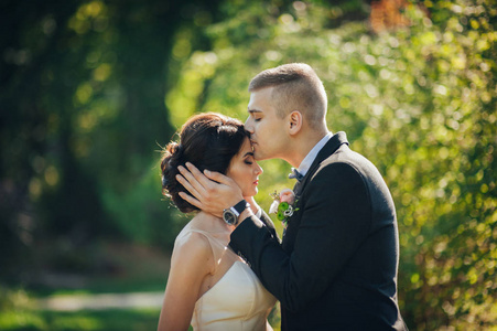 绿色的额头新郎亲吻新娘额头与绿色的树木背景照片
