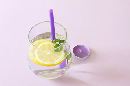 一杯水, 柠檬, 薄荷和蜡烛。玻璃纯净水和新鲜有机柠檬和薄荷分离在紫色背景和紫色蜡烛。排毒与健康食品概念