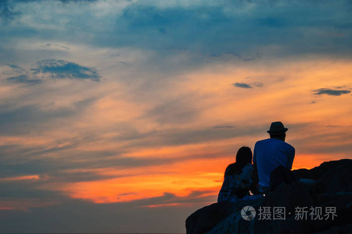 一个情侣的剪影坐在岩石上空, 傍晚的热带海, 在模糊的背景。夕阳柔和的背景与轻的公平