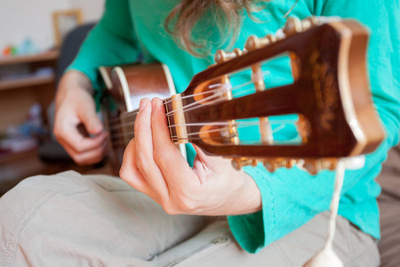 年轻人的手在家里演奏吉他四弦琴。在接近的视野中演奏四弦琴的男子