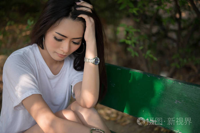 独自坐在公园长椅上的悲伤孤独的女人
