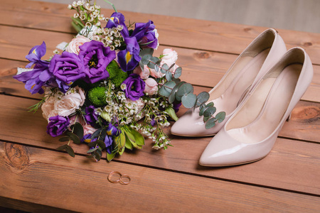 在一张木桌上, 带着绿叶紫色和白花的结婚花束, 结婚戒指