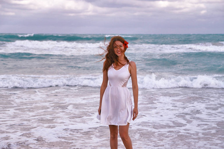海边的微笑的女孩。一个苗条, 被晒黑的女孩在白色礼服散步加勒比海波浪
