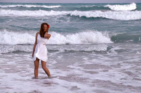 海边的微笑的女孩。一个苗条, 被晒黑的女孩在白色礼服散步加勒比海波浪