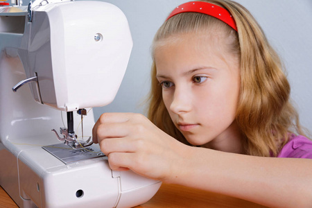 一个十几岁的女孩学会把针扎进现代缝纫机照片