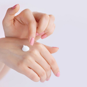 粉红色的指甲的年轻女子在她手上适用奶油