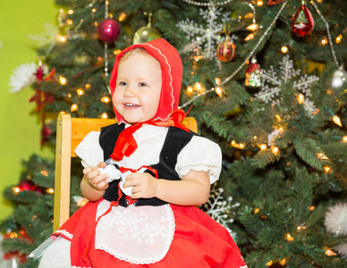 肖像的女孩子穿着一顶红色的帽子为各地一棵枞树的圣诞节装饰。孩子在假期新的一年