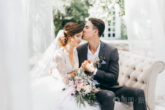 年轻的一对新婚夫妇摆姿势.新郎亲吻新娘