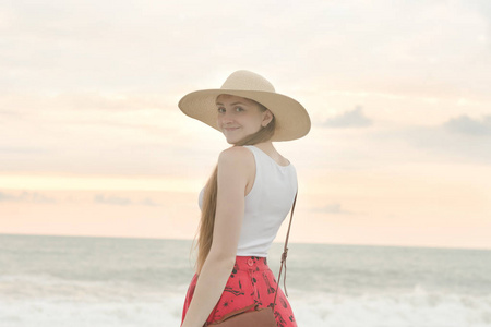 女孩在海滩上的帽子, 甜甜地微笑着。日落时间
