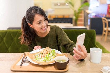 女人通过手机在餐厅以自拍照