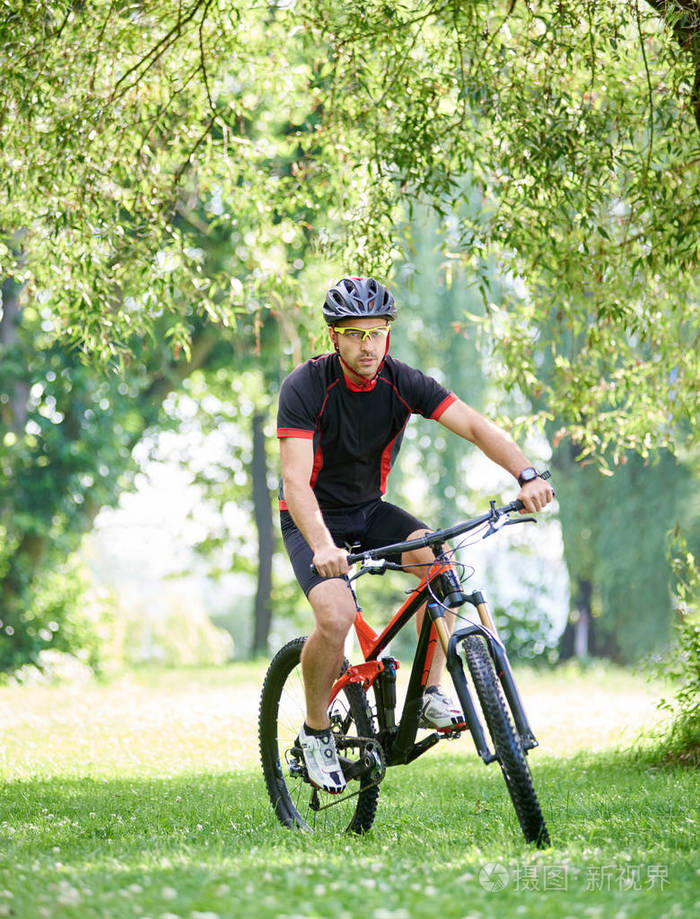 骑自行车的年轻人骑单车服和防护头盔, 沿着绿色公园小巷骑车.