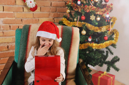 非常可爱的小宝贝女孩与小红盒子里的手放在圣诞树旁的椅子上