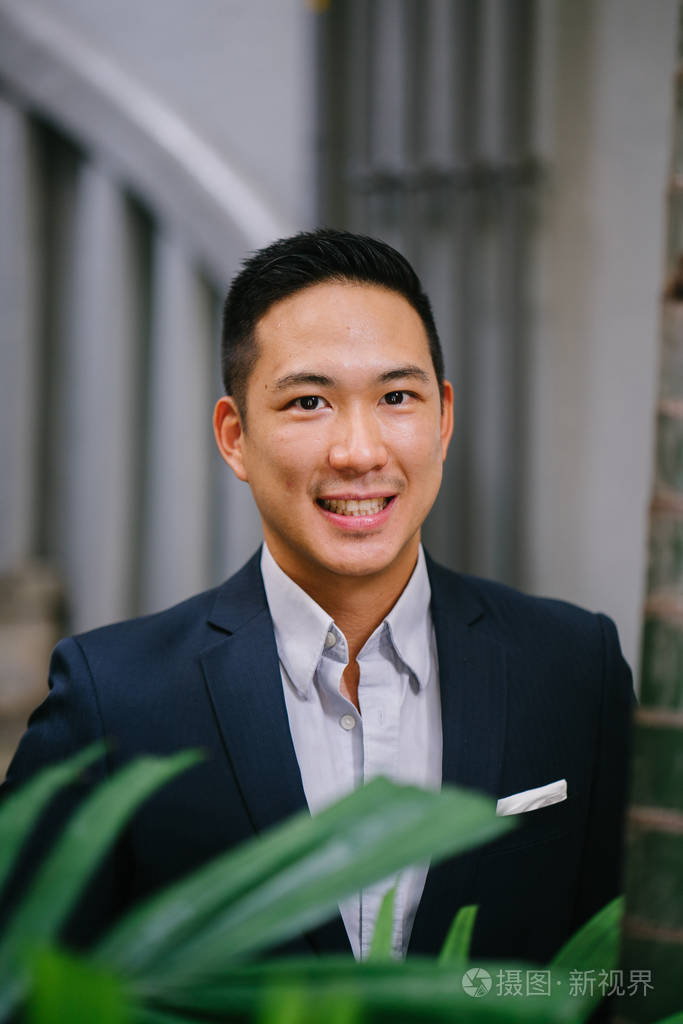 一个英俊, 年轻, 聪明的中国亚裔男子的肖像微笑着, 站在绿色的墙上的