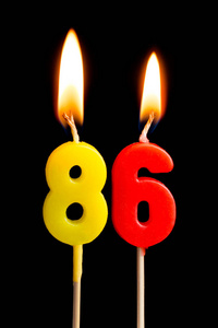 燃烧蜡烛的形式为86八十六 数字, 日期 的蛋糕孤立的黑色背景。庆祝生日周年纪念日重要日期节日餐桌设置的概念