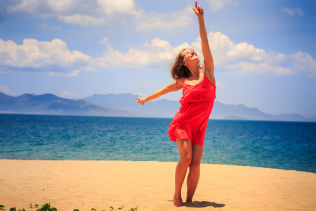 在红站在沙滩上的金发女孩举起手指向太阳