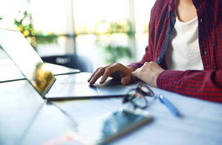 微笑着年轻的时髦男子在眼镜与笔记本电脑在桌子上.