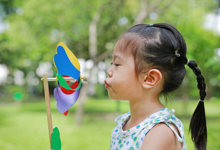 可爱的小女孩吹风力涡轮机在花园里