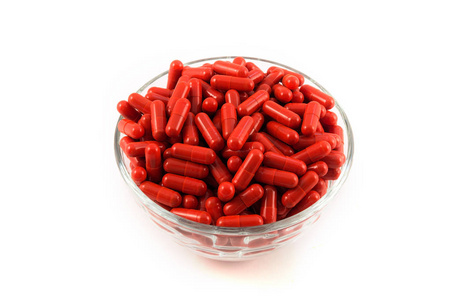 红色胶囊装满药, 在一个白色的背景玻璃杯堆积照片