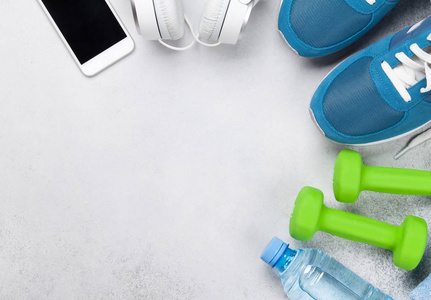 健身概念背景与运动鞋, 哑铃, 水瓶, 智能手机和耳机在石材背景。具有文本空间的顶部视图