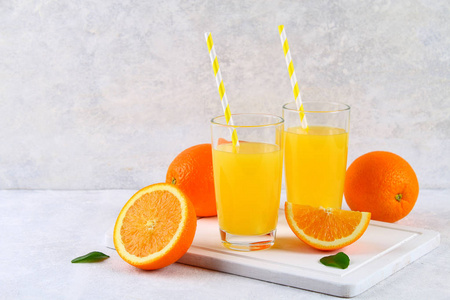 玻璃杯和一壶新鲜橙汁, 带橙色和黄色的切片, 在浅灰色的桌子上
