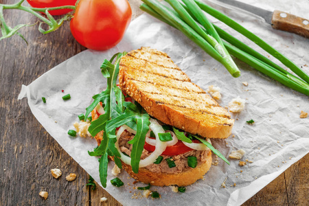 烤面包三明治配金枪鱼, 西红柿, 洋葱和芝麻菜。传统的健康食品由鱼蔬菜和烤面包制成。顶部视图