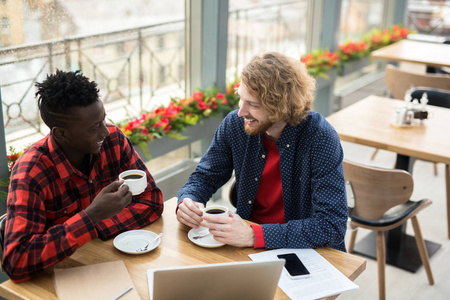 跨文化的青年男子坐在咖啡馆和商务谈话的杯茶