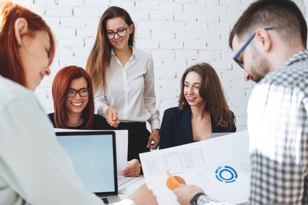 年轻的商业团队一起工作, 并在现代办公室使用笔记本电脑和纸图表和