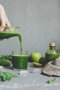 手把健康的绿色冰沙倒入罐子里。清洁饮食概念