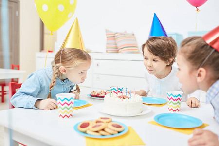 一群友好的孩子在蛋糕上吹蜡烛, 同时庆祝他们其中一个在幼儿园的生日