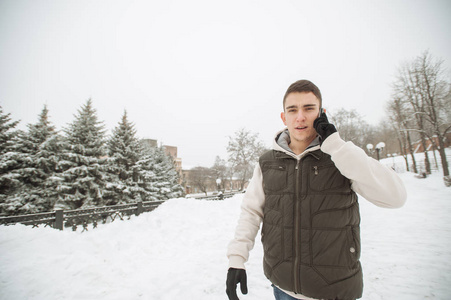 年轻英俊的男子，用电话的室外冬季肖像。他的夹克和背心摆在城市的街头，背景的杉树上的美丽少年