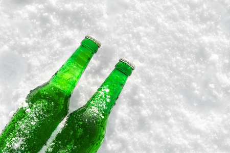 两瓶冰镇啤酒日落在雪地上。关闭了视图