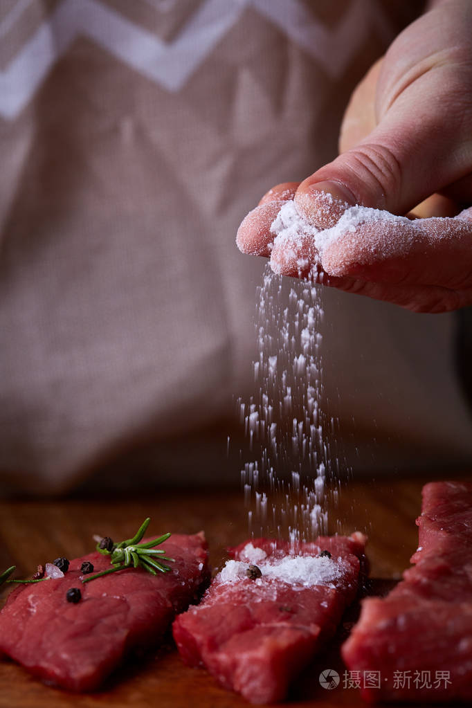 强大的专业人士手洒盐的生牛排, 选择性对焦, 特写